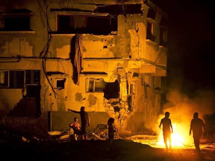 Members of two Palestinian families walk next to a fire amid destroyed homes on their block in Shejaiya on August 27, 2014. Shejaiya was one of the hardest hit neighborhoods in fighting between Hamas militants and Israel during 50 days of fighting. The fire was set by the home owners in an effort to keep mosquitoes away from their shattered homes. Israel and Palestinians both boasted of victory in the Gaza war but analysts say Hamas received only promises while the conflict aggravated divisions in the Israeli leadership. AFP PHOTO/ROBERTO SCHMIDT