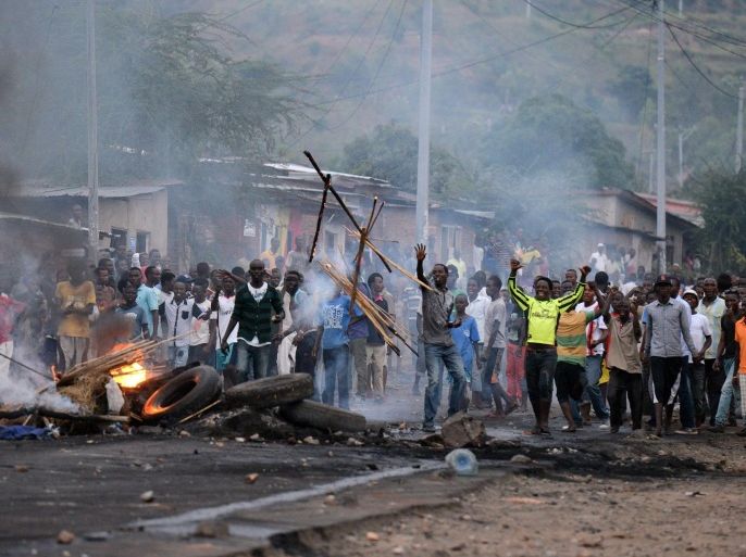 A man throws pieces of wood onto a barricade of burning wood and tires erected by protesters as they demonstrate against the president's bid for a third term in power in Musaga, in the outskirts of Bujumbura, on April 27, 2015. Police in Burundi battled protestors on April 27 in a second day of demonstrations over a bid by the central African nation's president for a third term in office. AFP PHOTO / SIMON MAINA