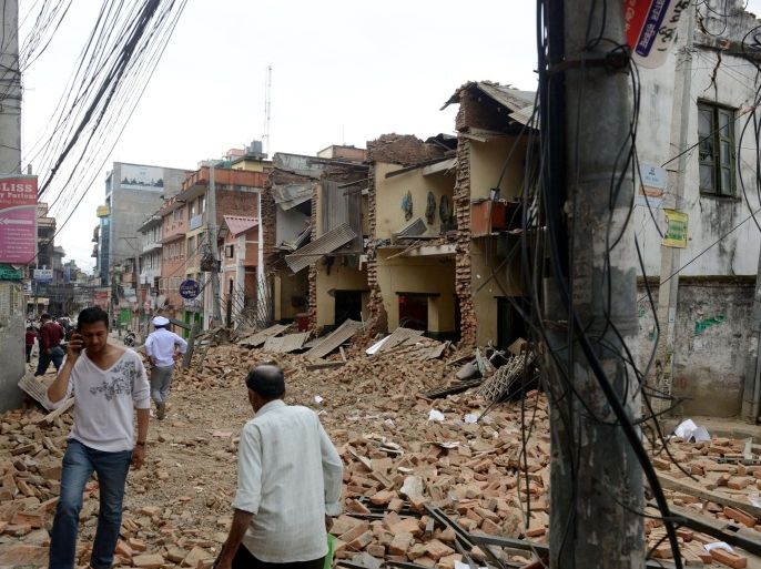 Nepalese people walk past collapsed buildings at Lalitpur, on the outskirts of Kathmandu on April 25, 2015.  A powerful 7.9 magnitude earthquake struck Nepal, causing massive damage in the capital Kathmandu with strong tremors felt across neighbouring countries.  AFP PHOTO / PRAKASH MATHEMA