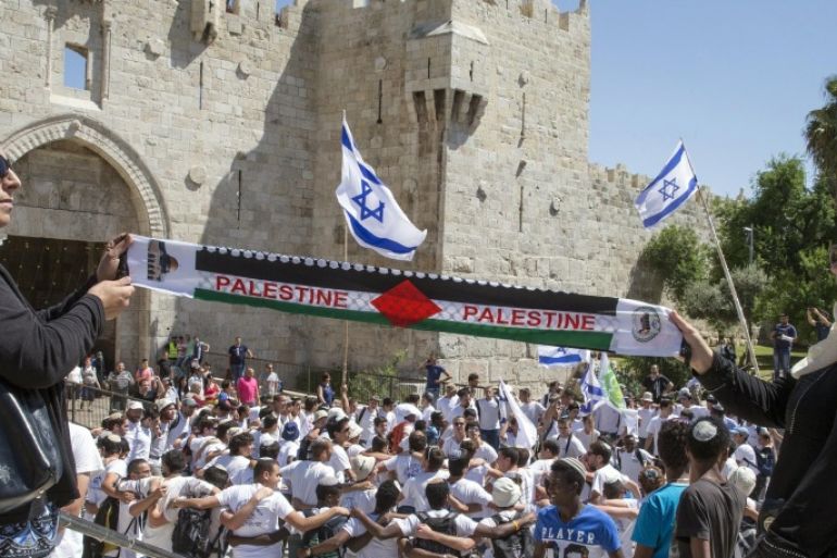 Palestinian women hold a scarf bearing the Palestine name as Israeli youths hold their national flag as they take part in the 'flag march' through Damascus Gate in Jerusalem's old city during celebrations for Jerusalem Day on May 17, 2015 which marks the anniversary of the 'reunification' of the holy city after Israel captured the Arab eastern sector from Jordan during the 1967 Six-Day War. AFP PHOTO / JACK GUEZ