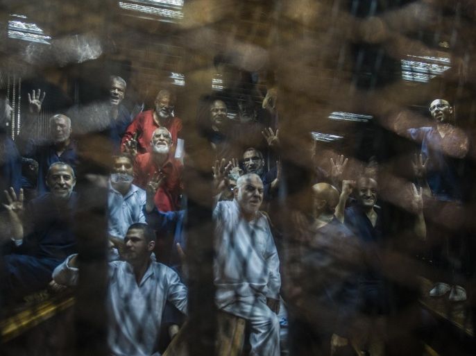 Egyptian Muslim Brotherhood leader Mohamed Badie (C-L) gestures from behind the defendant's cage as the judge reads out the verdict sentencing him and more than 100 other defendants, including Egypt's deposed Islamist president Mohamed Morsi, to death at the police academy in Cairo on May 16, 2015. AFP PHOTO / KHALED DESOUKI