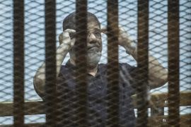 Ousted Egyptian president Mohamed Morsi, who was recently sentenced to death, gestures during his new trial in Cairo on May 23, 2015, with 25 other defendants including prominent Islamists and secular figures on trial for insulting the judiciary. AFP PHOTO / KHALED DESOUKI