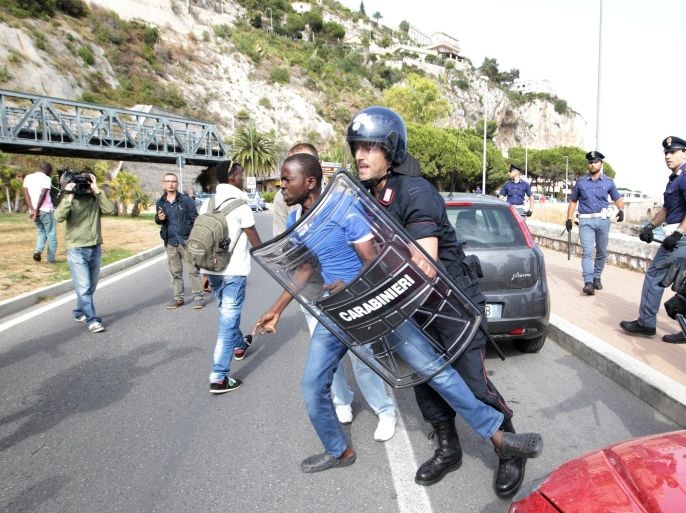 Italian policemen disperse migrants who were staging a sit-in at the border between Italy and France in the city of Ventimiglia, Italy, on June 13, 2015. The Italian police, wearing riot gear, tried to push around 200 migrants back towards the town of Ventimiglia, five kilometres (three miles) from the border, but a group of around 50 men took refused to comply and took refuge on nearby rocks. The Schengen open borders accord means migrants landing in Italy can usually easily travel through neighbouring France, Austria, Switzerland and Slovenia as they seek to make it to Britain, Germany and Scandinavia, but the G7 suspension of Schengen and a growing number of spot checks on buses and trains has made that harder, increasing the pressure on Italy, where reception facilities are at breaking point with some 76,000 people being accommodated nationwide. AFP PHOTO / JEAN-CHRISTOPHE MAGNENET