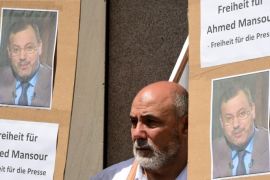 A man stands between posters with the portrait of Al-Jazeera journalist Ahmed Mansour during a demonstration for his release in front of the local court of Berlin's Tiergarten district, where Mansour is being held in custody, awaiting a judge's decision on his further detention, on June 21, 2015. In the case that has raised issues about press freedom and German relations with Egypt under President Abdel Fattah al-Sisi, Mansour was arrested Saturday (June 20, 2015) at a Berlin airport having been accused by Cairo of committing 'several crimes'. AFP PHOTO / JOHN MACDOUGALL