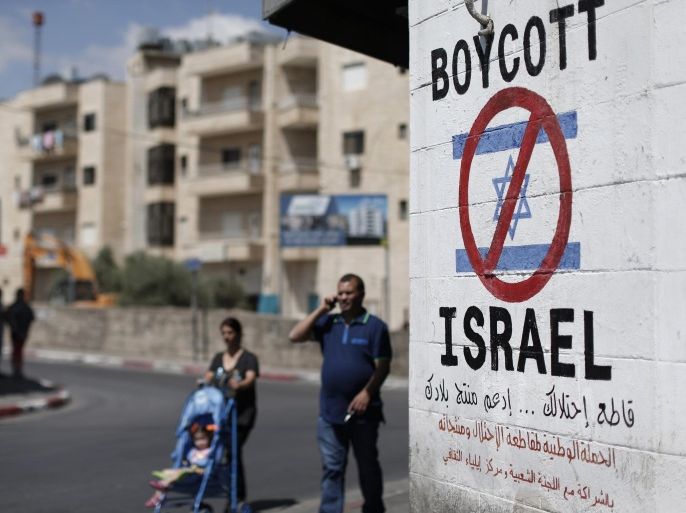 Palestinians walk past a sign painted on a wall in the West Bank biblical town of Bethlehem on June 5, 2015, calling to boycott Israeli products coming from Jewish settlements. The international BDS (boycott, divestment and sanctions) campaign, that pushes for a ban on Israeli products, aims to exert political and economic pressure over Israel's occupation of the Palestinian territories in a bid to repeat the success of the campaign which ended apartheid in South Africa. AFP PHOTO / THOMAS COEX