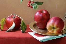 Fresh picked apples on table by vase of flowers and metal goblet