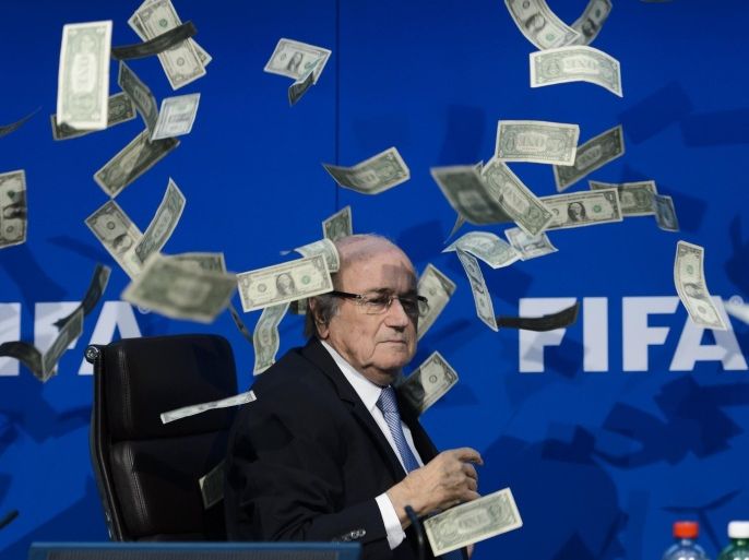 FIFA president Sepp Blatter looks on with fake dollars note flying around him thrown by a protester during a press conference at the football's world body headquarter's on July 20, 2015 in Zurich. FIFA said today that a special election will be held on February 26 to replace president Sepp Blatter. AFP PHOTO / FABRICE COFFRINI