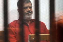 CAIRO, EGYPT - JUNE 27: Former Egyptian President Mohamed Morsi, wearing a red uniform after Cairo Criminal Court sentenced him to death over a prison break in 2011, stands behind bars during the trial of him and ten others for allegedly 'espionage for Qatar' at Cairo Police Academy on June 27, 2015 in Cairo, Egypt.
