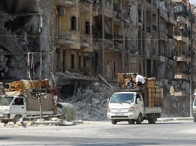 Men drive pick-up trucks past damaged buildings as they transport furniture in the old city of Aleppo, Syria August 24, 2015. REUTERS/Abdalrhman Ismail