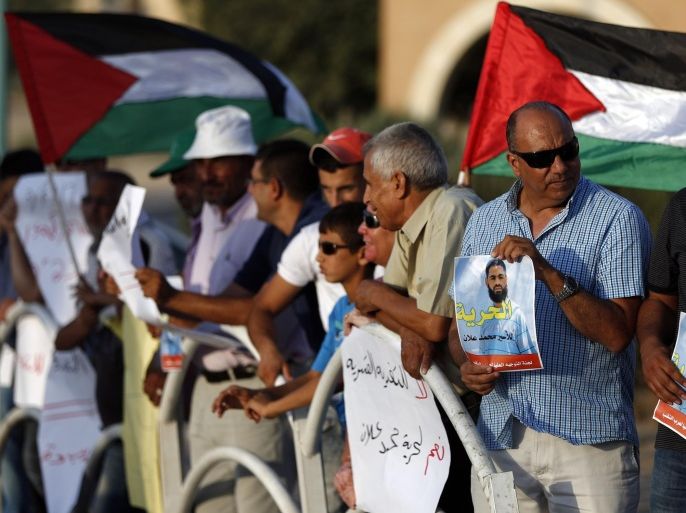 Arab-Israeli protesters wave Palestinian flags and hold posters of Mohammed Allan, a Palestinian prisoner who is on a long-term hunger strike, during a rally calling for his release in the southern Israeli Bedouin city of Rahat on August 18, 2015. Allan, who has been on hunger strike for the past two months, emerged from a coma on August 18 but pledged to resume fasting if Israel did not resolve his case within 24 hours, a Palestinian group said. AFP PHOTO / AHMAD GHARABLI