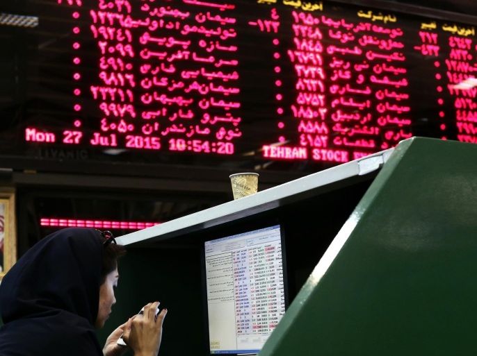 An Iranian dealer checks her mobile phone next to stock market activity boards at the stock exchange in the capital Tehran on July 27, 2015. Iran's central bank chief said that Iran has assets of $29 billion in overseas banks that could be unlocked under a nuclear deal struck on July 14, far less than reported estimates of over $100 billion. AFP PHOTO / BEHROUZ MEHRI
