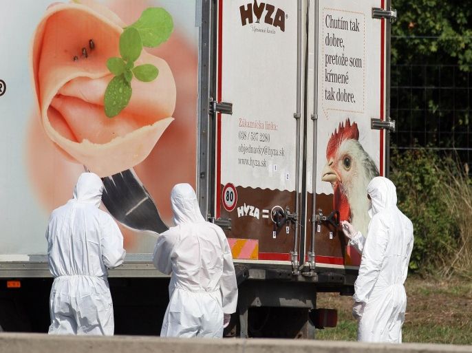 Investigators stand near a truck that stands on the shoulder of the highway A4 near Parndorf south of Vienna, Austria, Thursday, Aug 27, 2015. At least 20 migrants were found dead in the truck parked on the Austrian highway leading from the Hungarian border, police said. (AP Photo/Ronald Zak)