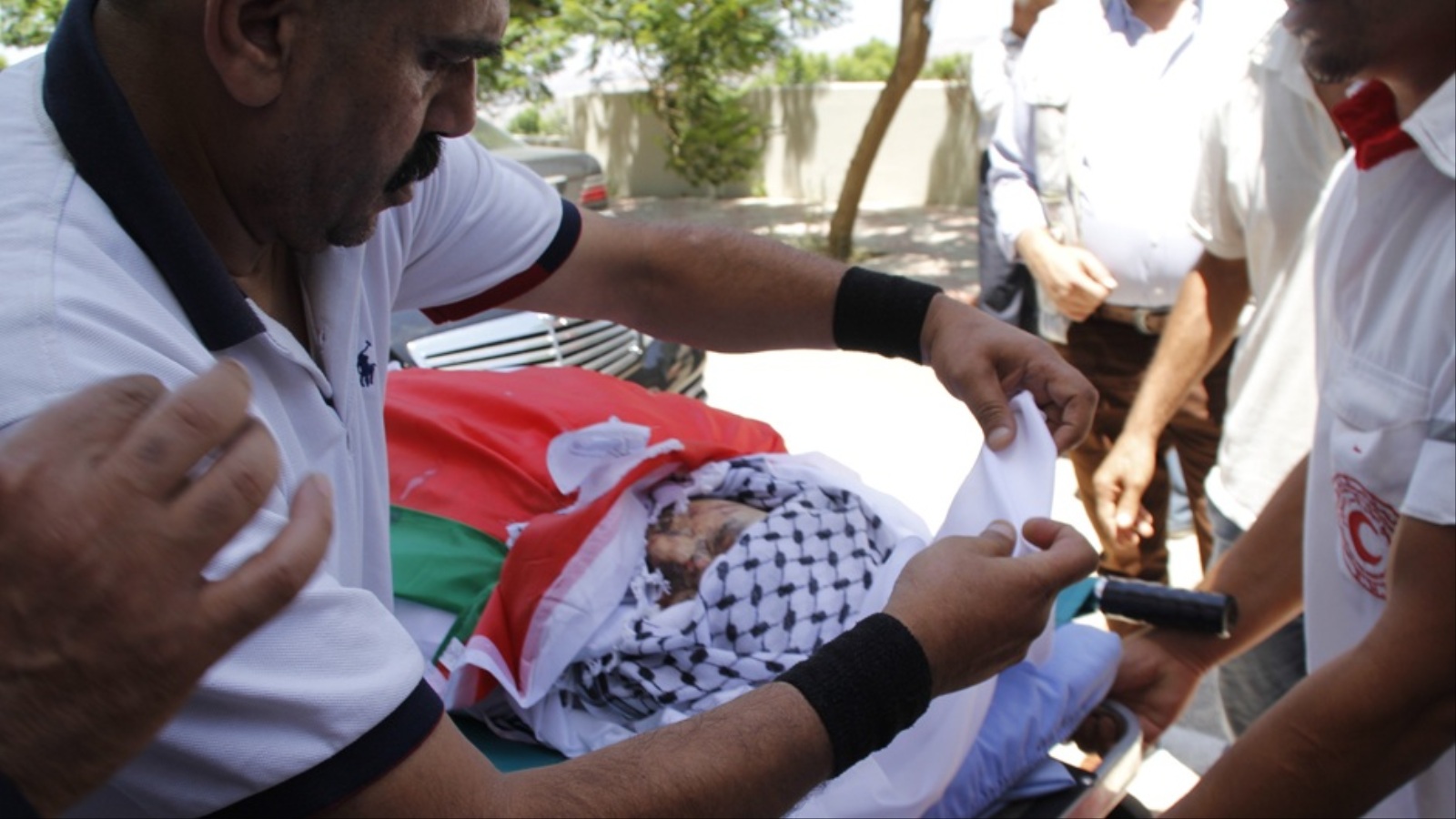 ‪ضابط إسعاف يحاول تغطية الشهيد سعد دوابشة قبيل تشييعه‬  (الجزيرة نت)