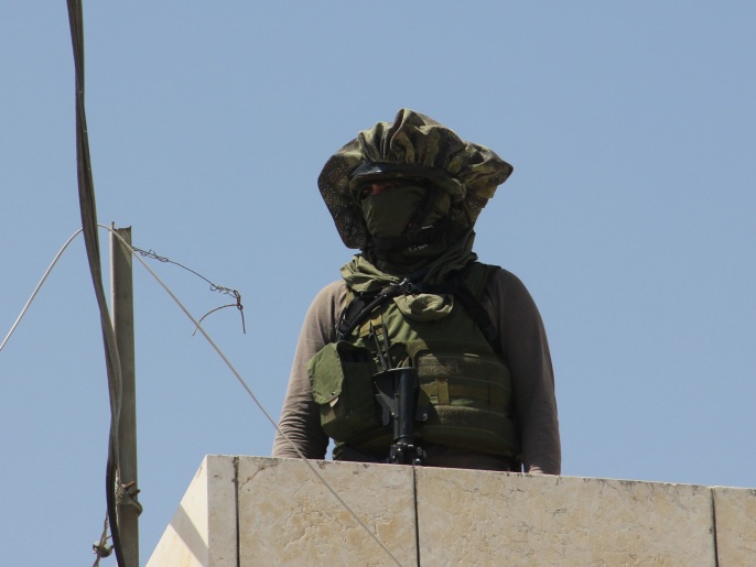 جندي إسرائيلي مقنع يعتلي سطح مبنى فلسطيني بمدينة الخليل (الجزيرة)