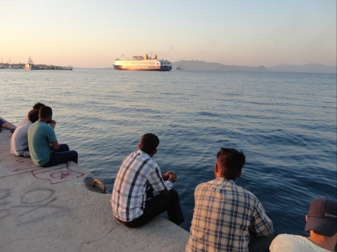 اليونان- جزيرة كوس، الشاطئ، مهاجرون بانتظار أوراقهم، يراقبون من على شاطئ الجزيرة، باخرة مسافرة الى اثينا