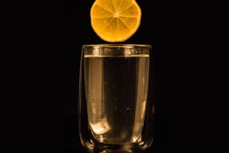 Sliced Lemon Over Glass Of Water Against Black Background