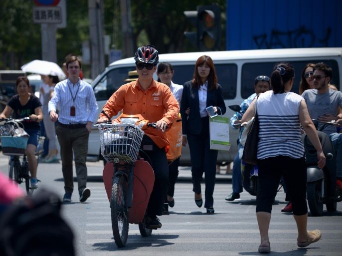 A courier (C) rides his electric bicycle while crossing the street in Beijing on July 13, 2015. China's total trade slumped in the first half of this year, official data showed on July 13, falling well short of the government's targets and dealing a blow to the global economy from its biggest trader in goods. AFP PHOTO / WANG ZHAO