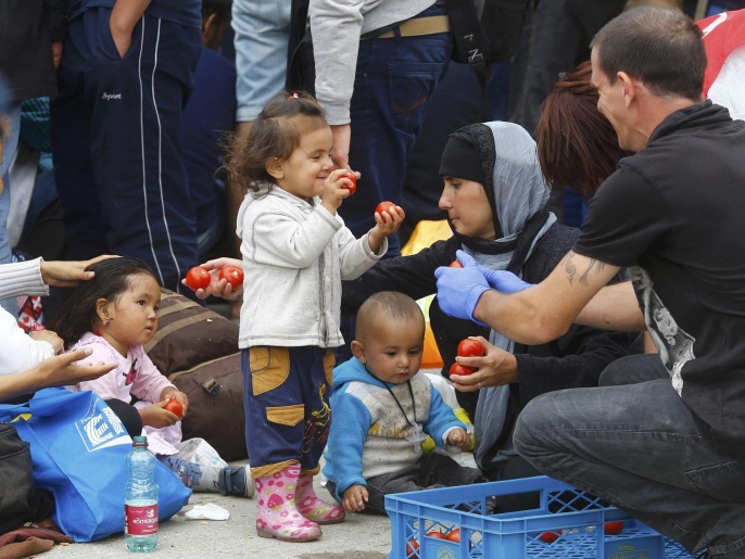 ‪(رويترز)‬ أطفال يتلقون بعض الفواكه خلال انتظار الحافلات بنقطة على الحدود المجرية النمساوية
