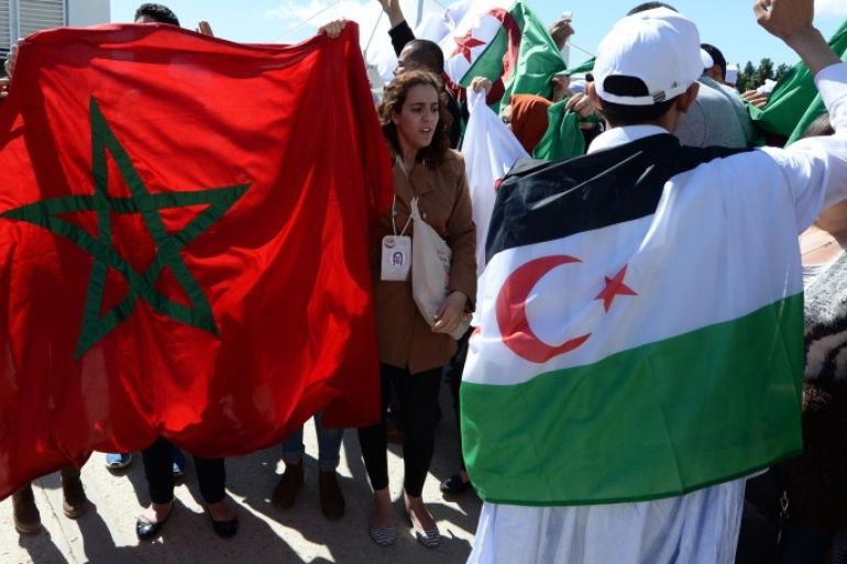 Moroccan activists wave their national flag (L) next to an Algieran man bearing the flag of the Polisario Front seperatist movement, as international activists shout slogans during the World Social Forum (WSF) in Tunis on March 25, 2015. The WSF is an annual meeting of civil society organisations which gives social movements the opportunity for open debate and promotes international solidarity. The Polisario Front is an armed movement, backed by Algeria, which is fighting for the independence of the Western Sahara after it was annexed by Morocco in 1976 following Spain's withdrawal. AFP PHOTO / FADEL SENNA
