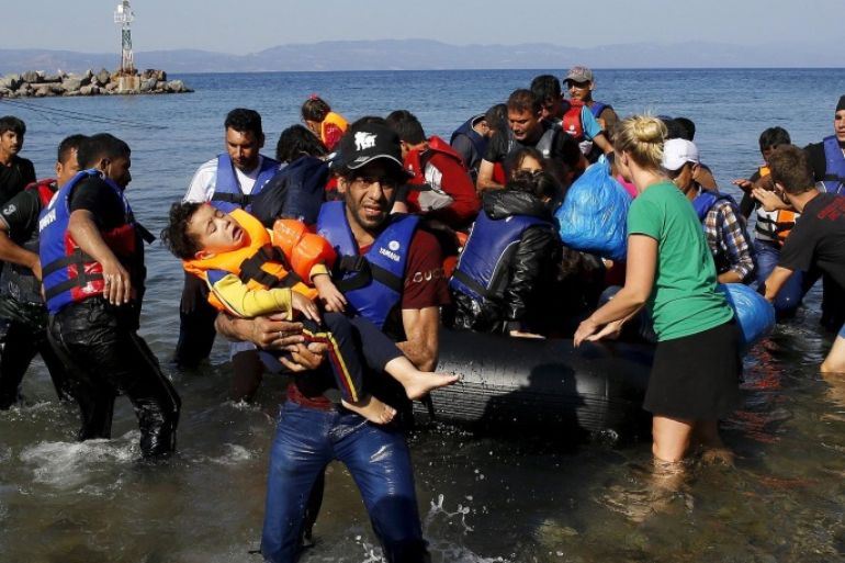 A Syrian refugee carries his child at a beach on the Greek island of Lesbos after crossing part of the Aegean Sea from the Turkish coast, September 19, 2015. A girl believed to be five years died on Saturday and 13 other migrants were feared lost overboard after their boat sank in choppy seas off the Greek island of Lesbos, the Greek coastguard said. A second, exhausted group of around 40 people reached the island in a small boat following a traumatic journey from Turkey, having paddled through the night with their hands across 10 kilometers (six miles) of ocean after their engine failed. Hundreds of thousands of mainly Syrian refugees have braved the short but precarious crossing from Turkey to Greece's eastern islands this year, mainly in flimsy and overcrowded inflatable boats. REUTERS/Yannis Behrakis