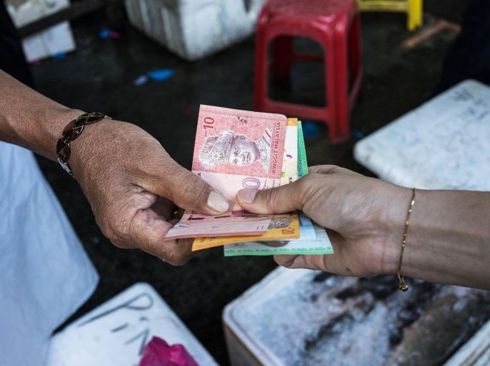 A fishmonger hands Malaysian ringgit banknotes to a customer at a market in the Pandamaran area of Klang, Selangor, Malaysia, on Wednesday, May 27, 2015. Malaysia's ringgit fell for a sixth day on June 1, in the longest stretch of losses since 2013 as falling oil prices weigh on the nation's finances.