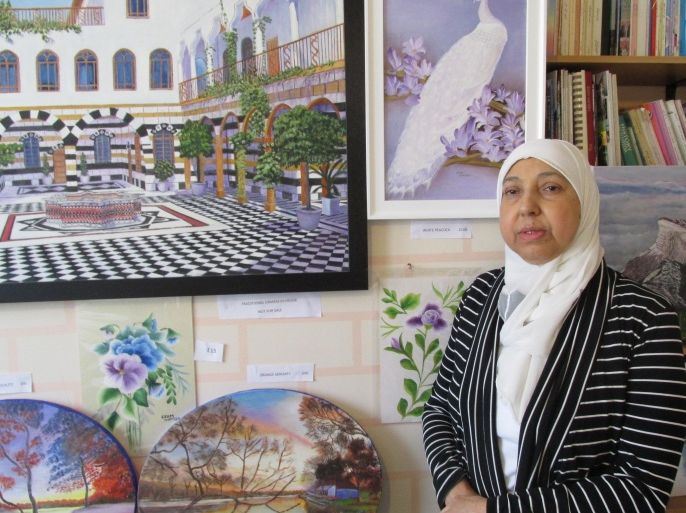 الفنانة عصام حمزة داخل منزلها وخلفها لوحاتتها ورسوماتها