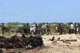 Jubaland forces and Somali residents stand near the site of a suicide car bomb attack near a military training base in the port town Kismayu, south of capital Mogadishu August 22, 2015. A suicide car bomb was rammed into a military training base in the Somali port city of Kismayu on Saturday, killing "many soldiers", officials said. Residents said they heard a loud blast followed by gunfire. Military officials said the attack was launched as soldiers were lining up for training. REUTERS/Abdiqani Hassan