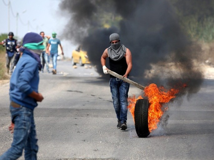 A Palestinian protester fuels a burning barricade with a tire during clashes with Israeli security forces in near Al Fawar Refugee camp near Hebron city, 20 October 2015. UN Secretary General Ban Ki-moon will urge calm during a visit on 20 October 2015 to Israel and the West Bank as he seeks to end more than two weeks of the worst street violence in years.