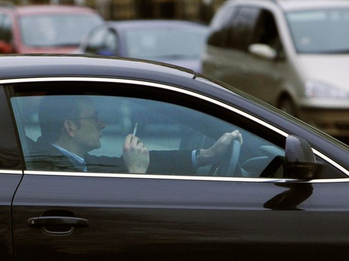 A driver sits in his car with a lit cigarette at traffic lights in Edinburgh, Scotland March 24, 2010. Smokers should be banned from lighting up in all private cars as part of stricter laws to protect children from passive smoking, a doctors' group said in a report on Wednesday.