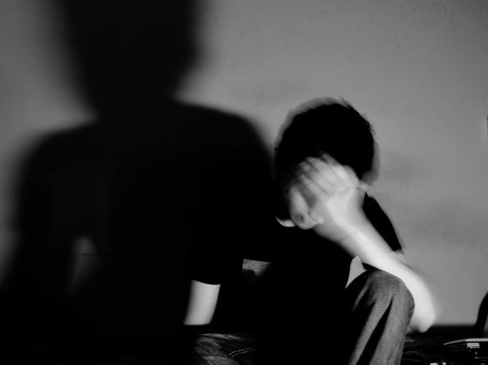 Depressed Man Sitting With Head In Hands Against Wall