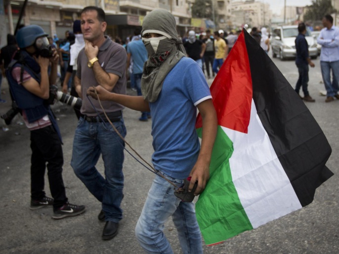 ‪شاب فلسطيني يحمل علم بلاده قبل يومين قرب حاجز قلنديا بين القدس ورام الله‬ (غيتي)