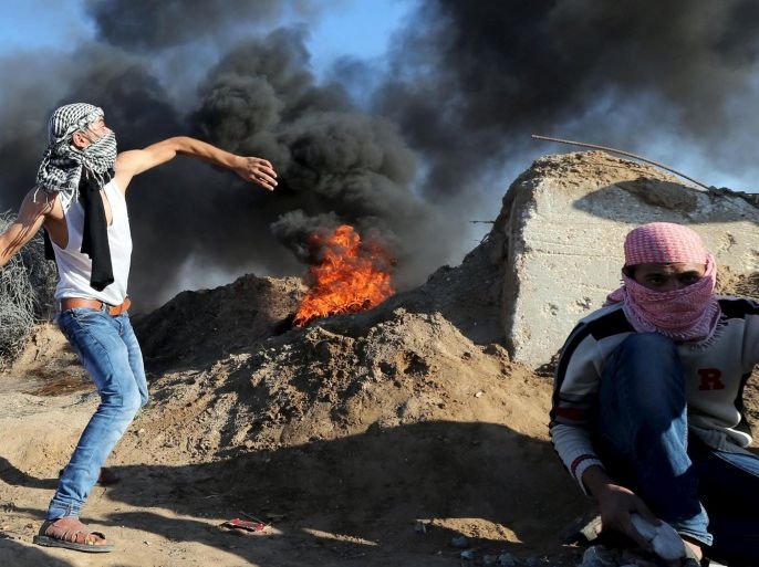 A Palestinian protester hurls stones towards Israeli troops as another takes cover during clashes near the border between Israel and Central Gaza Strip October 30, 2015. Knife-wielding Palestinians attacked Israelis in Jerusalem and the Israeli-occupied West Bank on Friday and one assailant was shot dead, police said, extending a wave of violence spurred in part by tensions over a Jerusalem holy site. REUTERS/Ibraheem Abu Mustafa