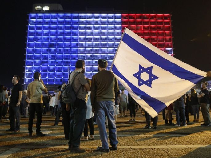People hold the Israeli national flag as the Tel Aviv Municipality building light is illuminated in the colours of the French national flag as people gather to show solidarity for the victims of the 13 November Paris attacks in Rabin's square in Tel Aviv, Israel, 14 November 2015. More than 120 people have been killed in a series of attacks in Paris on 13 November, according to French officials.