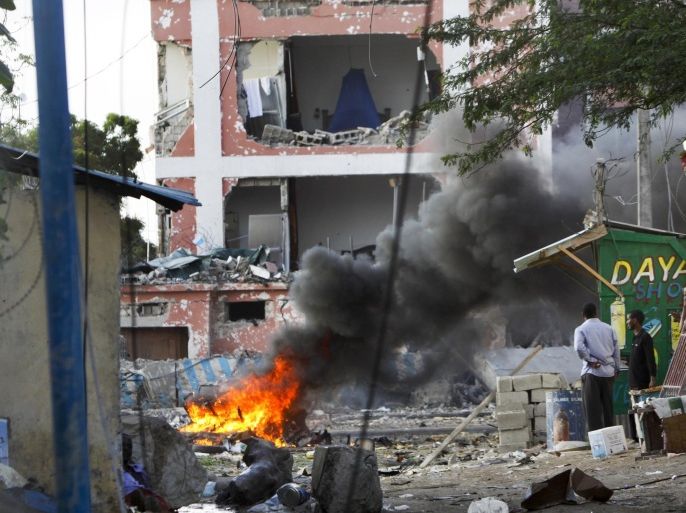 Somali men watch as fires burn amidst the destruction outside the Sahafi Hotel in Mogadishu, Somalia Sunday, Nov. 1, 2015. A Somali police officer says an explosion followed by heavy gunfire has been heard, thought to have been caused by a suicide car bomb, at the hotel often frequented by Somali government officials and business executives. (AP Photo/Farah Abdi Warsameh)