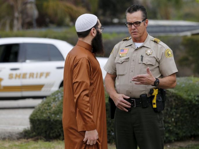 A San Bernardino police officer talks with a member of the mosque, where shooting suspect Syed Rizwan Farook was seen two to three times a week at lunch time, at the road side entrance to the mosque in San Bernardino, California December 4, 2015. Authorities are investigating the San Bernardino, California, shooting as an "act of terrorism", Federal Bureau of Investigation assistant director David Bowdich said at a news conference on Friday. REUTERS/Mike Blake