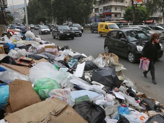 In this Thursday, Dec. 17, 2015 photo, a Lebanese woman covers her nose from the smell as she passes by a pile of garbage on a street in Beirut, Lebanon. Lebanon’s trash collection crisis which set off summer protests is entering its sixth month, but you would hardly be able to know it in Beirut. (AP Photo/Bilal Hussein)