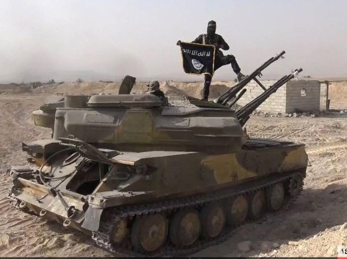 FILE - In this file photo released on Aug. 5, 2015, by the Rased News Network a Facebook page affiliated with Islamic State militants, an Islamic State militant holds the group's flag as he stands on a tank they captured from Syrian government forces, in the town of Qaryatain southwest of Palmyra, central Syria. Decades of reckless arms trading and poorly regulated arms flow into Iraq have contributed to the Islamic State group's "large and lethal arsenal" being used to commit war crimes on a massive scale in Iraq and Syria, an international rights group said Tuesday, Dec. 8. (Rased News Network via AP, File)