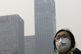 A woman wearing a face mask to protect herself from pollutants walks past office buildings shrouded with pollution haze in Beijing, Monday, Dec. 7, 2015. Beijing issued its first-ever red alert for smog on Monday, urging schools to close and invoking restrictions on factories and traffic that will keep half of the city's vehicles off the roads. (AP Photo/Andy Wong)