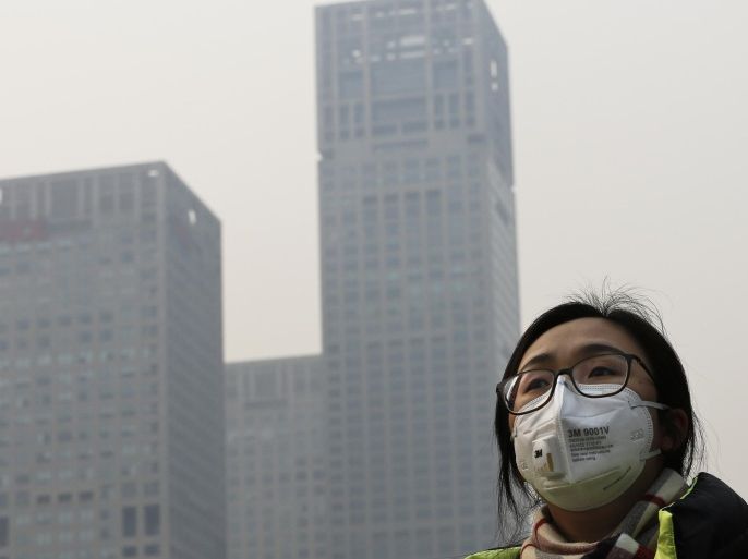 A woman wearing a face mask to protect herself from pollutants walks past office buildings shrouded with pollution haze in Beijing, Monday, Dec. 7, 2015. Beijing issued its first-ever red alert for smog on Monday, urging schools to close and invoking restrictions on factories and traffic that will keep half of the city's vehicles off the roads. (AP Photo/Andy Wong)