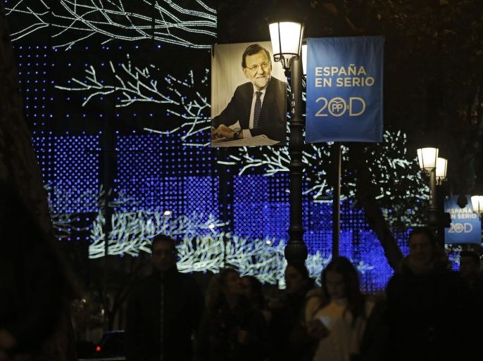People walk past under a campaign poster with a photograph of Popular Party leader and current Prime Minister of Spain Mariano Rajoy and with a slogan in Spanish: "Spain: Seriously", in Madrid, Saturday, Dec. 19, 2015. The Spanish general elections will be held on Sunday, Dec. 20. (AP Photo/Francisco Seco)