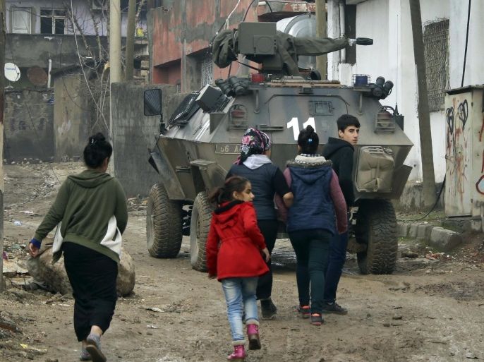 Backdropped by a Turkish forces armoured personnel carrier, residents walk around after the 24-hour curfew was lifted, in the mostly-Kurdish town of Silopi, in southeastern Turkey, near the border with Iraq, Tuesday, Jan. 19, 2016. Turkey's prime minister announced Tuesday that military operations against Kurdish rebels have ended in one mainly Kurdish southeastern town. The military is still fighting militants linked to the Kurdistan Workers' Party, or PKK, in two other urban areas. (AP Photo/Mahmut Bozarslan)