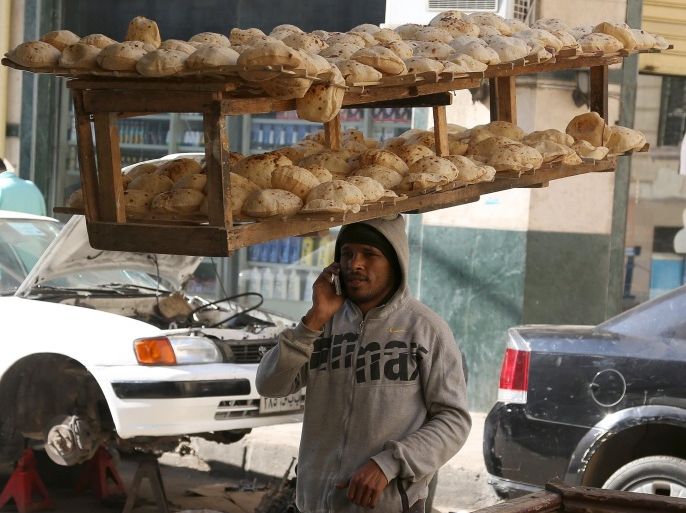 An employee of a bakery talks on his mobile while balancing on his head a tray of freshly baked bread from a local bakery in a street in Cairo, Egypt, January 12, 2016. REUTERS/Asmaa Waguih