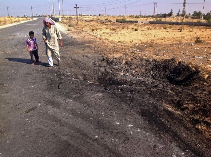 FILE - In this Nov. 20, 2013 file photo, a man and child walk past a crater from a suicide car bomb attack on the road between the border town of Rafah and the coastal city of el-Arish, Egypt. Egyptian authorities on Tuesday, Oct. 28, 2014, ordered residents living along the country's eastern border with the Gaza Strip to evacuate so they can demolish their homes and set up a buffer zone to stop weapons and militant trafficking between Egypt and the Palestinian territory, officials said. The measure comes four days after militants attacked an army post, killing at least 31 soldiers in the restive area in the northeastern corner of the Sinai Peninsula. (AP Photo/Ahmed Abu Deraa, File)