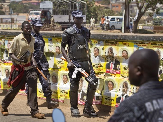 An armed Ugandan riot policeman patrols past campaign posters for long-time President Yoweri Museveni, as well as local members of Parliament, on a street in Kampala, Uganda Wednesday, Feb. 17, 2016. On the eve of presidential elections, a heavy police and military presence can be seen in the capital Kampala. (AP Photo/Ben Curtis)