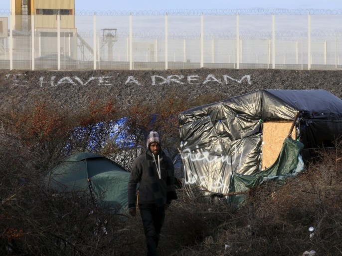 A migrant walks between makeshift shelters near an embankment with the message, "We Have A Dream" below a fence topped with razor wire in the "new jungle", a field where migrants and asylum seekers gather in Calais, France, in this December 30, 2015 file photo. REUTERS/Pascal Rossignol/Files
