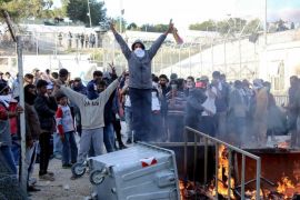 Migrants make a victory sign as garbage bins burn at the Moria migrant detention center on the northeastern Greek island of Lesbos, Tuesday, April 26, 2016. A protest broke out in Moria during a visit there by the Greek migration affairs minister and a Dutch official, with protesters, mainly unaccompanied teenagers, setting fires and riot police on standby. (Petros Tsakmakis/InTime News via AP)