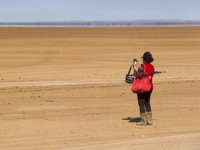 A South African woman takes a picture with her cellphone on the Hakskeenpan during the 2014 Kalahari Desert Speedweek at Hakskeenpan, Northern Cape of South Africa, 24 September 2014. Dubbed the Woodstock of motorsports events the Speedweek sees enthusiasts gathering in a remote desert in the north of the country to commune and drive their vehicles across seven kilometers of specially prepared clay track for high speed top end runs. Technically the desert Speedweek is more challenging than asphalt requiring much more driving and engineering skills for top honours in each class. Hakskeenpan in the Northern Cape of South Africa close to the Namibian border is where the British Bloodhound rocket powered car will attempt to set the new world land speed record of 1610km/h in 2015.