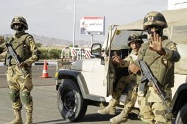 FILE - In this Friday, Nov. 6, 2015 file photo, Egyptian soldiers guarding the entrance to the Sharm el-Sheikh International Airport gesture to a photographer in south Sinai, Egypt. The sign has a picture of Egyptian President Abdel-Fattah el-Sissi and a slogan in Arabic which reads, "Long Live Egypt." Startling public criticism in Egypt points to how the aura of invincibility that President Abdel-Fattah el-Sissi has long enjoy appears to be eroding. The criticisms spring from multiple fronts _ complaints over neglect by officials, an economy that hasn’t seen dramatic improvement and now worries over tourism following the crash of a Russian jet in Sinai. (AP Photo/Thomas Hartwell, File)