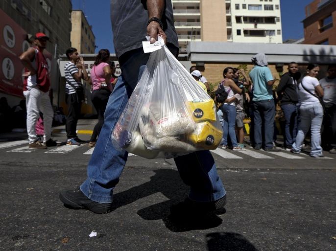 A man walks out of a supermarket carrying corn flour, rice and mayonnaise in a plastic bag, while others wait in line to try to buy staple items in Caracas January 16, 2016. Venezuela's socialist government decreed an "economic emergency" on Friday that will expand its powers and published the first data in a year that shows the depth of a recession fueled by low oil prices and a sputtering state-led model. The central bank, which has been lambasted by critics of Presi
