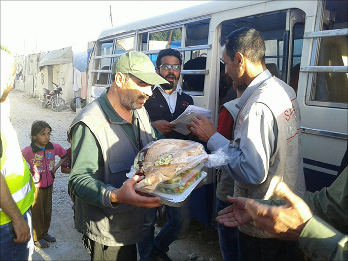 أعضاء جمعة سوا للتنمية والإغاثة والمتطوعون يوزعون وجبات الإفطار على اللاجئين (الجزيرة)
